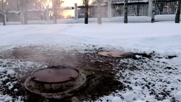 Close-up steam is from sanitary sewer cover in snow in winter park. Melted snow around. — Stock Video