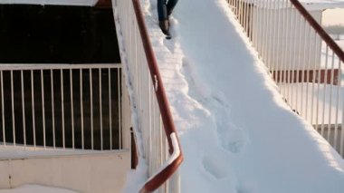 Mavi bir ceket kürk başlık ile kadın almak karlı bir merdiven. Önden görünüm.