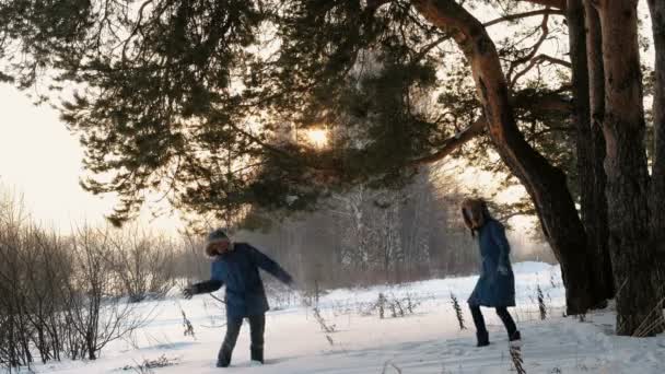 Homem e mulher jogando bolas de neve na floresta de inverno. Pôr do sol na floresta de inverno . — Vídeo de Stock