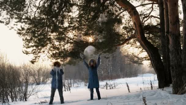 Homme et femme vêtus de doudounes bleues jettent de la neige dans la forêt hivernale et sourient. Vue de face — Video