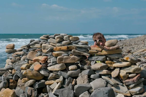 男孩玩, 躲在海岸边海滩上的石头堡垒后面. — 图库照片