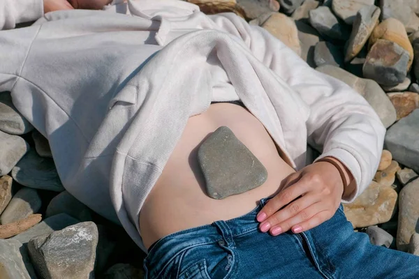 Stein auf dem Bauch der Mädchen. Unerkennbares Mädchen liegt im Herbst an einem Steinstrand. — Stockfoto