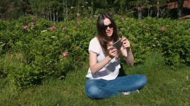 Kadın parkta oturan güneşli bir günde cep telefonunda bir oyun oynuyor.