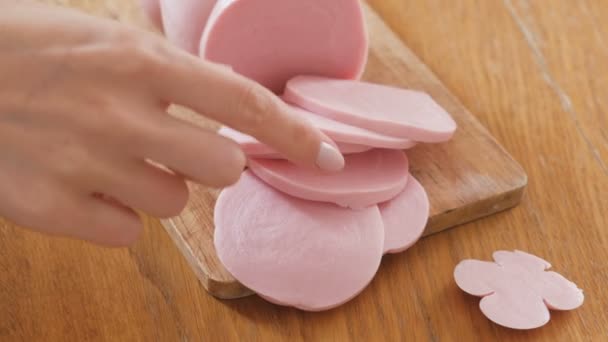 Vrouw neemt segmenten van een gekookte worst op houten snijplank op de keukentafel. Close-up handen. — Stockvideo