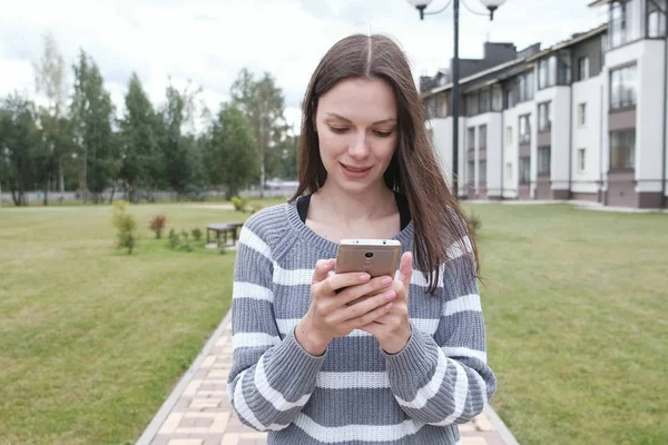Vakker brunettdame leser noe på mobilen i nærheten av hjemmet . – stockfoto