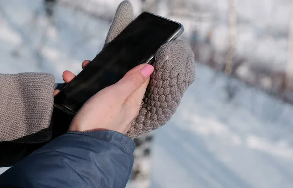 Крупным планом женщины в рукавицах пишут сообщения на сотовом в зимнем парке . — стоковое фото