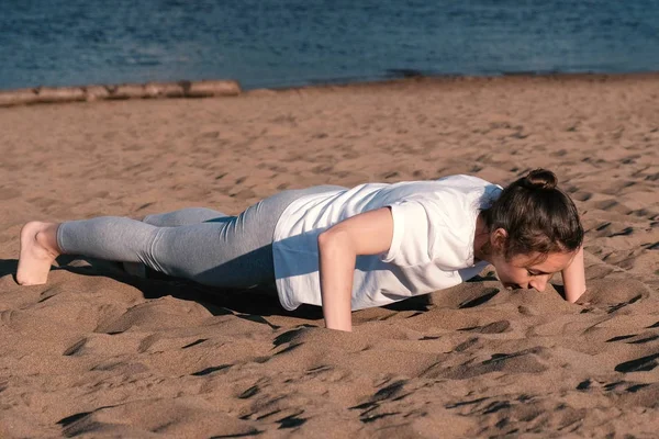 Kvinnan gör övningar sport på stranden av floden i staden. Squeezings. — Stockfoto