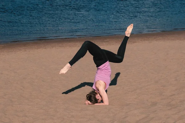 在城市的河边在海滩上做瑜伽的女人。美丽的景色。倒立. — 图库照片