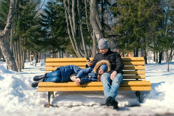 Homem e uma mulher descansam juntos em um banco no parque da cidade de inverno . — Fotografia de Stock