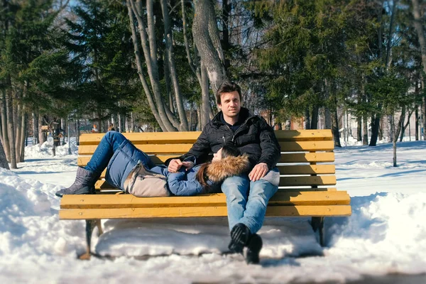 Homem e uma mulher descansam juntos em um banco no parque da cidade de inverno. Dia de inverno ensolarado . — Fotografia de Stock