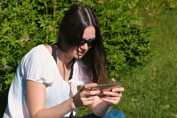 Mujer está jugando un juego en el teléfono móvil sentado en el parque en el día soleado . — Foto de Stock