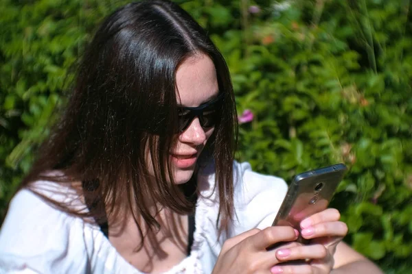 Женщина печатает сообщение на мобильном телефоне, сидя в парке в солнечный день, болтая . — стоковое фото