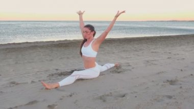 Genç kadın yan bölmeleri içinde kumsalda güneş doğarken oturan yoga yaparken.