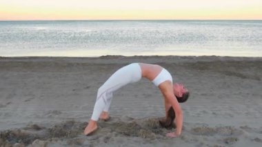 Genç kadın Chakrasana tekerlek poz kumlu plajda güneş doğarken germe yoga yaparken.