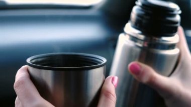 Bir fincan sıcak çay ve kışın arabada oturan termos tutarak kadının el closeup görünümü.