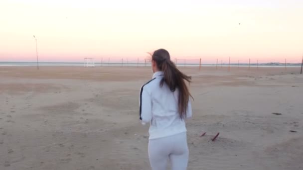 Mladá žena je běhání na písčité pláži u moře při západu slunce v podzimní, zadní pohled. — Stock video
