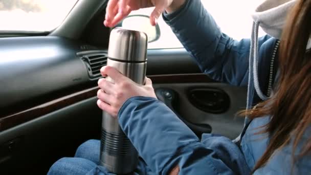 Unrecognizable woman pouring a hot tea in a cup from thermos and drinking it sitting in the car in winter. — Stock Video