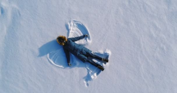 Vrouw maakt sneeuw engel in de sneeuw te leggen. Luchtfoto video. — Stockvideo