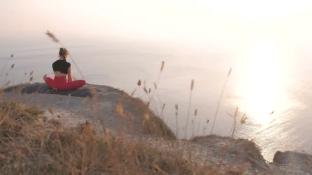 Vacker utsikt över kvinnan gör yoga Baddha Konasana bunden vinkel Pose på berget med utsikt över havet vid solnedgången. Bakifrån. — Stockvideo