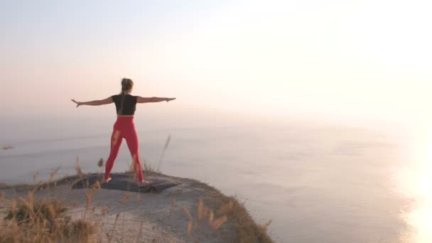 Bela vista da mulher fazendo ioga alongamento na montanha com vista para o mar ao pôr do sol . — Vídeo de Stock