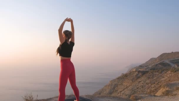 Krásný pohled na ženu dělá jógu, strečink na hoře s výhledem na moře při západu slunce. Natahovat ruce nahoru. — Stock video