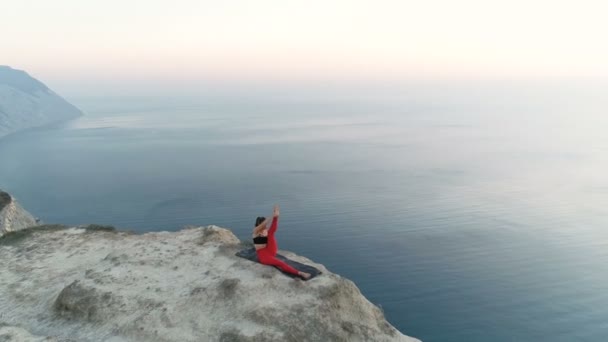 Прекрасний вид на жінку робить йогу Нантасану, Підйом ноги на горі з видом на море на заході сонця Повітряні кадри . — стокове відео