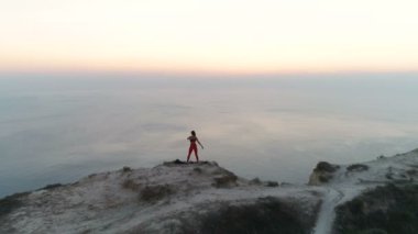 Güzel kadın yoga stretcing ve gün batımında deniz manzaralı dağ üstüne meditasyon yapıyor. Havadan görüntüleri. Arkadan görünüm.
