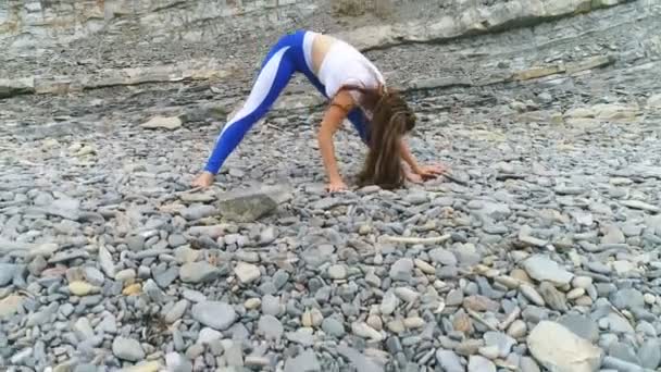 Kadın yoga ve rock ve deniz arka plan üzerinde fiziksel egzersizler yapıyor. Hava güzel görüntüleri görünümü. — Stok video