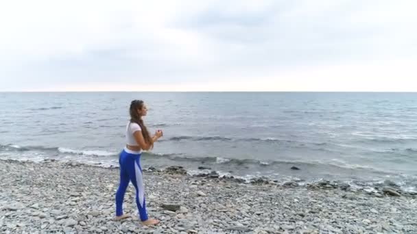 Κορίτσι κάνει άσκηση για τα πόδια του bodyflex κατά αναπνοή ασκήσεις στο παρασκήνιο στη θάλασσα και το βράχο. Εναέρια βίντεο. — Αρχείο Βίντεο