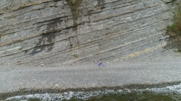 女性は岩と海の背景にヨガや stretcing の練習をしています。空中の美しい映像サイドビュー. — ストック動画