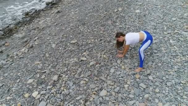 Жінка робить йогу і розтягує вправи на кам'яному і морському фоні. Повітряний красивий вигляд кадрів . — стокове відео