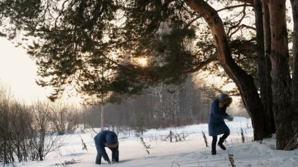Hombre y mujer jugando bolas de nieve en el bosque de invierno. Puesta de sol en el bosque de invierno . — Vídeos de Stock