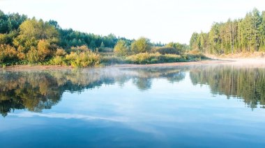 Nehri üzerinde sis. Sonbahar orman nehir kıyısındaki suya yansıyan.