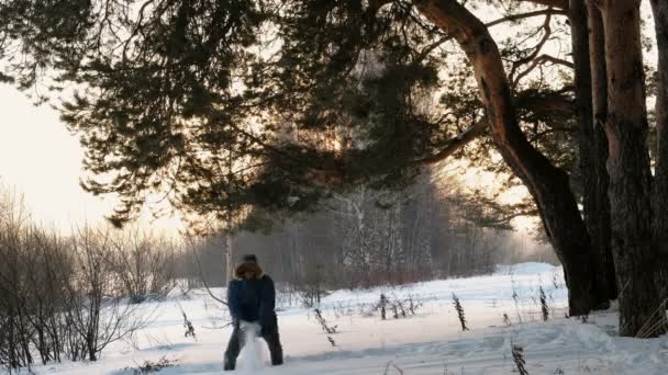 O homem joga neve na floresta de inverno ao pôr-do-sol. Vista frontal . — Vídeo de Stock