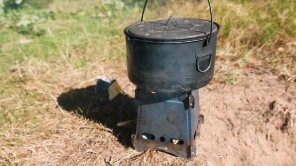 Pot on a metal camp furnace stove on woods outdoors. — Stock Video