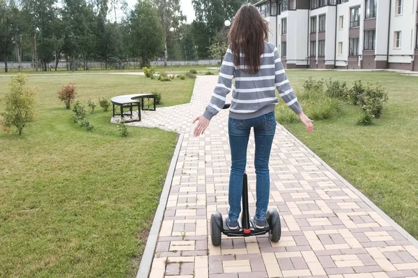 Morena mujer está rodando en scooter giroscopio cerca de la casa, vista trasera . —  Fotos de Stock