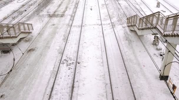 Залізниці в снігу на залізничній станції серед сходів, вид зверху, камера рухається вперед . — стокове відео