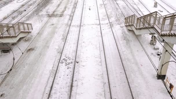 Ferrovias na neve na estação de trem entre as escadas, vista superior, câmera avançar . — Vídeo de Stock