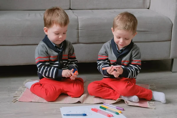 Two twin brothers toddlers draw together markers sitting on the floor.