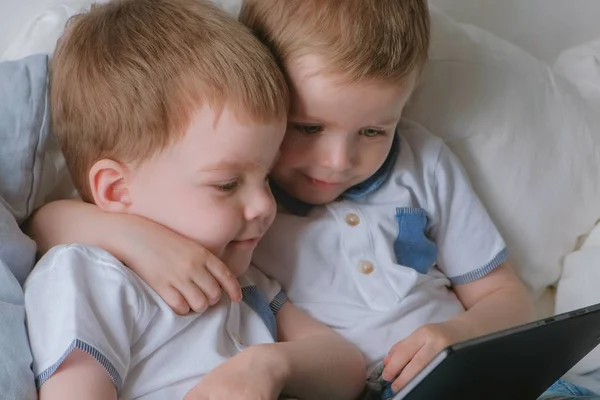 Niños con tableta. Dos niños gemelos niños pequeños mirando dibujos animados en la tableta acostado en la cama . — Foto de Stock