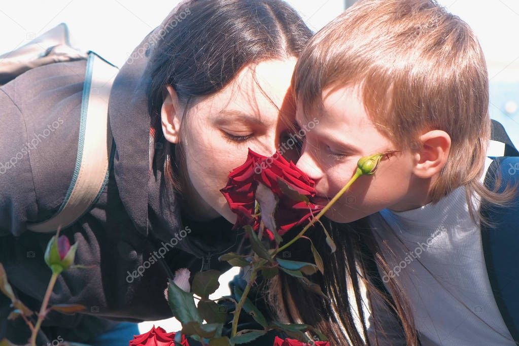 Mother and son together sniffing a rose.