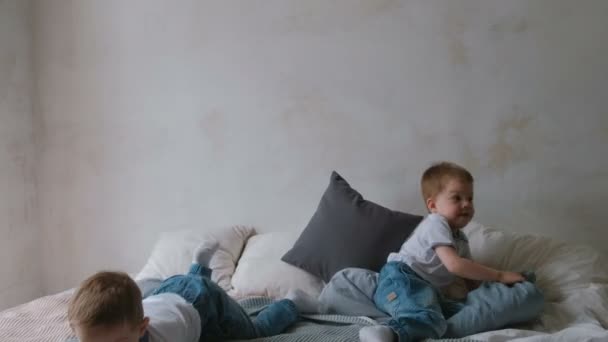 Двоє хлопчиків лягають на ліжко, кидають подушки, стрибають і сміються . — стокове відео