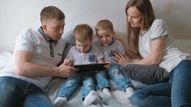 Familia con tableta. Mamá, papá y dos hijos gemelos niños pequeños mirando dibujos animados en la tableta acostado en la cama . — Vídeo de stock