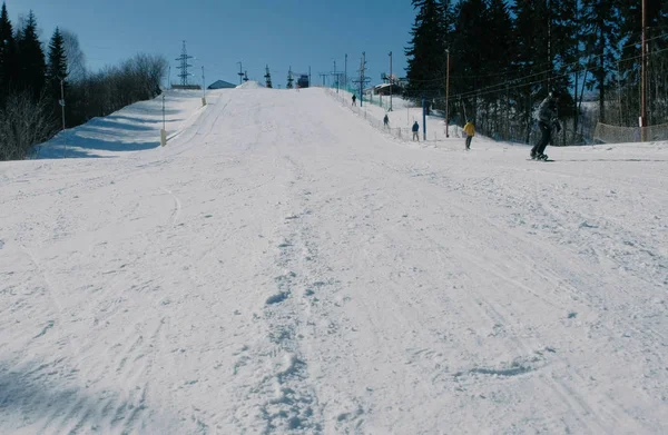 La gente che fa scorrere su uno snowboard da discesa di neve vicino sky lift. Vista da lontano . — Foto Stock