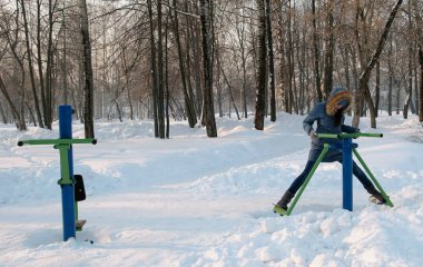 Kadın mavi ceket kukuleta ile aşağı bacak egzersizleri simülatör kışın Park Önden Görünüm yapıyor