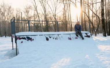 Adam paten kar yatılı parkta oturuyor. Kar üstünde belgili tanımlık tepe kaykay sürükleniyor. Bulanıklık