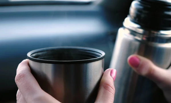 Widok zbliżenie womans rąk utrzymanie kubek gorącej herbaty i termos, siedząc w samochodzie, w zimie. — Zdjęcie stockowe