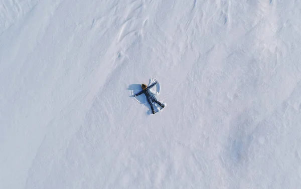 Vrouw maakt sneeuw engel in de sneeuw te leggen. Bovenaanzicht. Luchtfoto foto. — Stockfoto