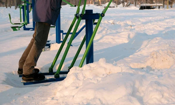 Makro mans nogi robi ćwiczenia na symulatorze w winter Park w mieście. Widok z boku. — Zdjęcie stockowe