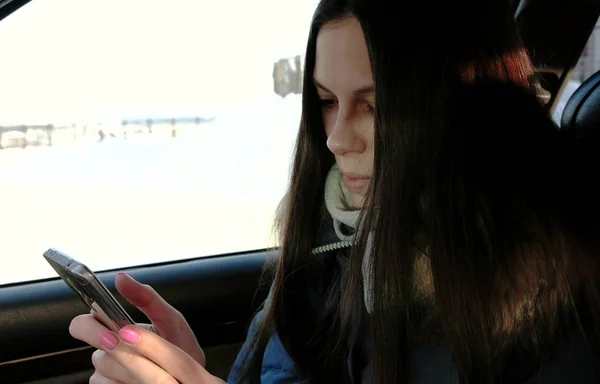 Una mujer de cerca chateando su celular sentada en el auto. Vista lateral . — Foto de Stock